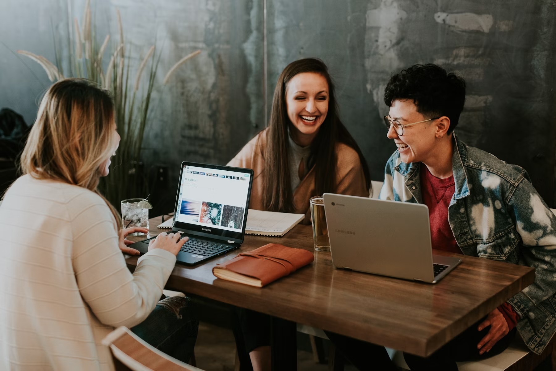 Three college students laughing together over a phone at a coffee shop